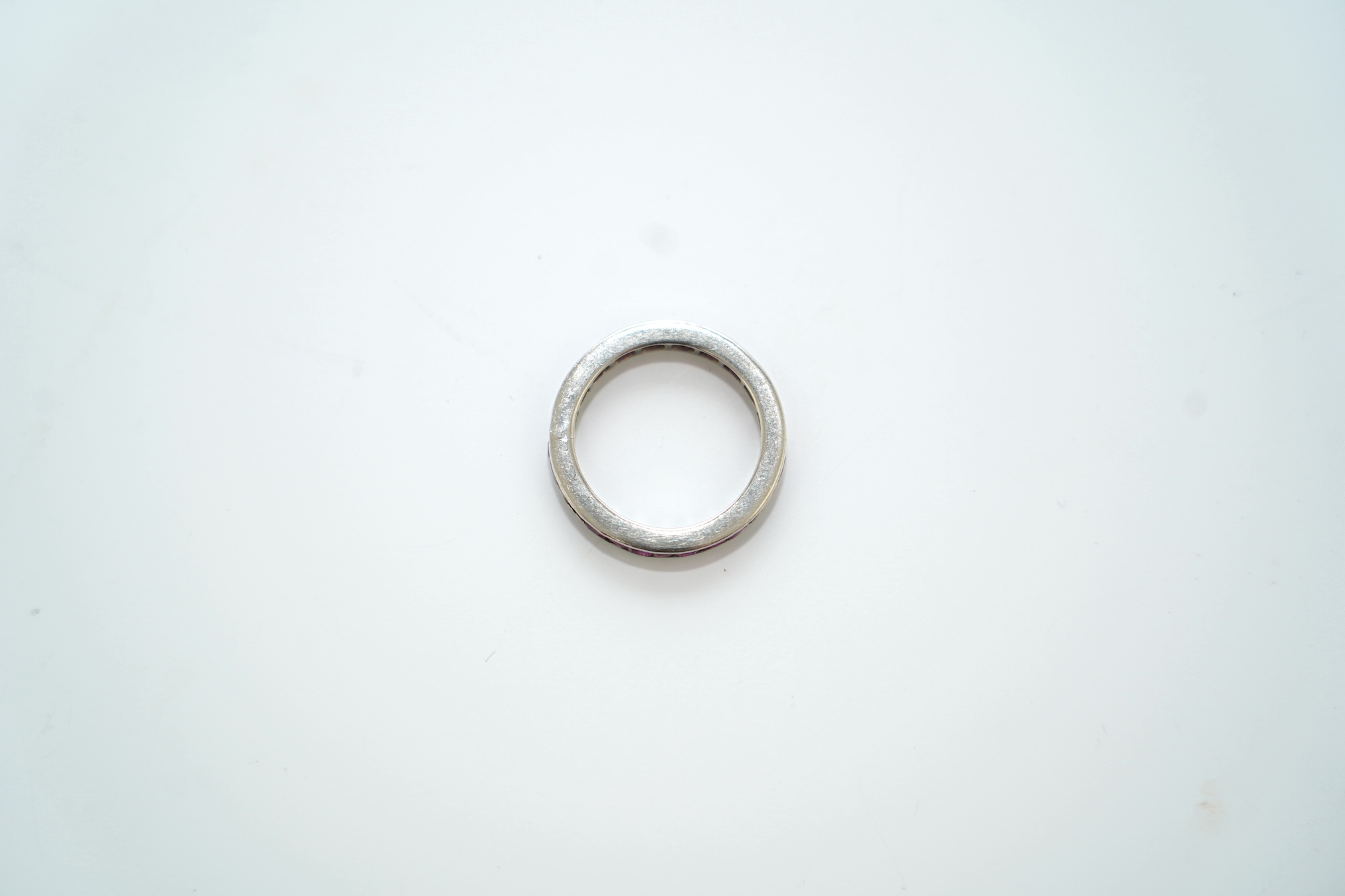 A white metal and rectangular cut ruby set full eternity ring, size M/N, gross weight 3.5 grams. Condition - fair